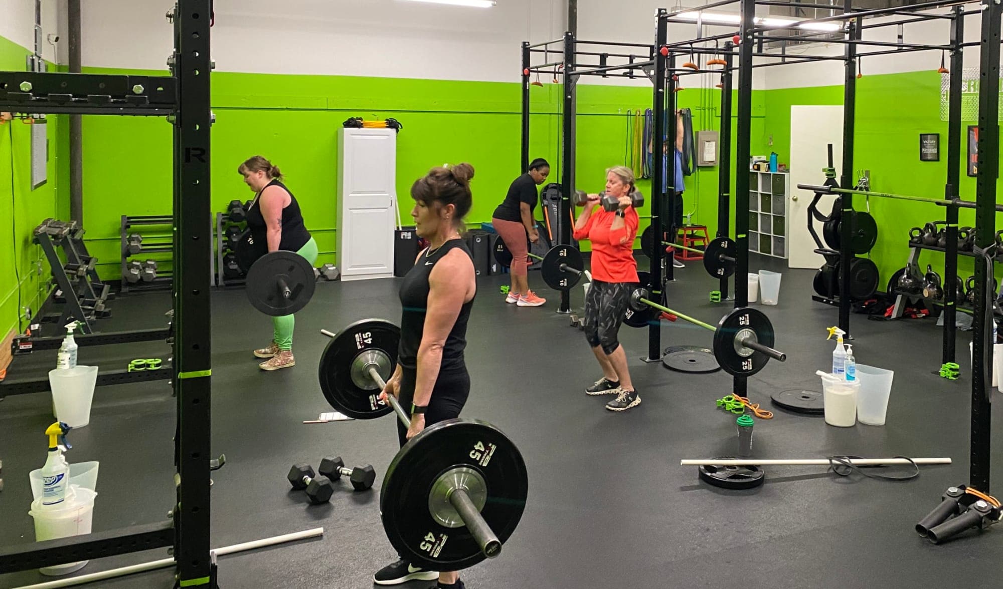 A small group of women deadlifting barbells with a coach at Create Fitness